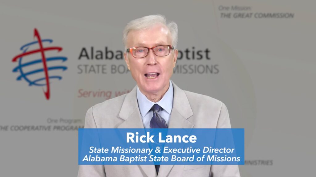 Dr. Rick Lance standing in front of a white background with the ALSBOM logo on it.